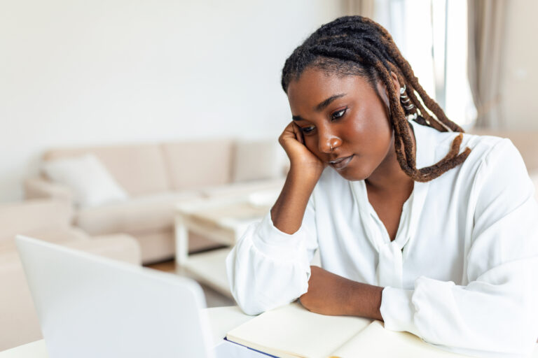 Serious frowning African American ethnicity woman sit at workplace desk looks at laptop screen read e-mail feels concerned
