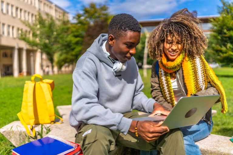 Students using laptop sitting at campus in a sunny day